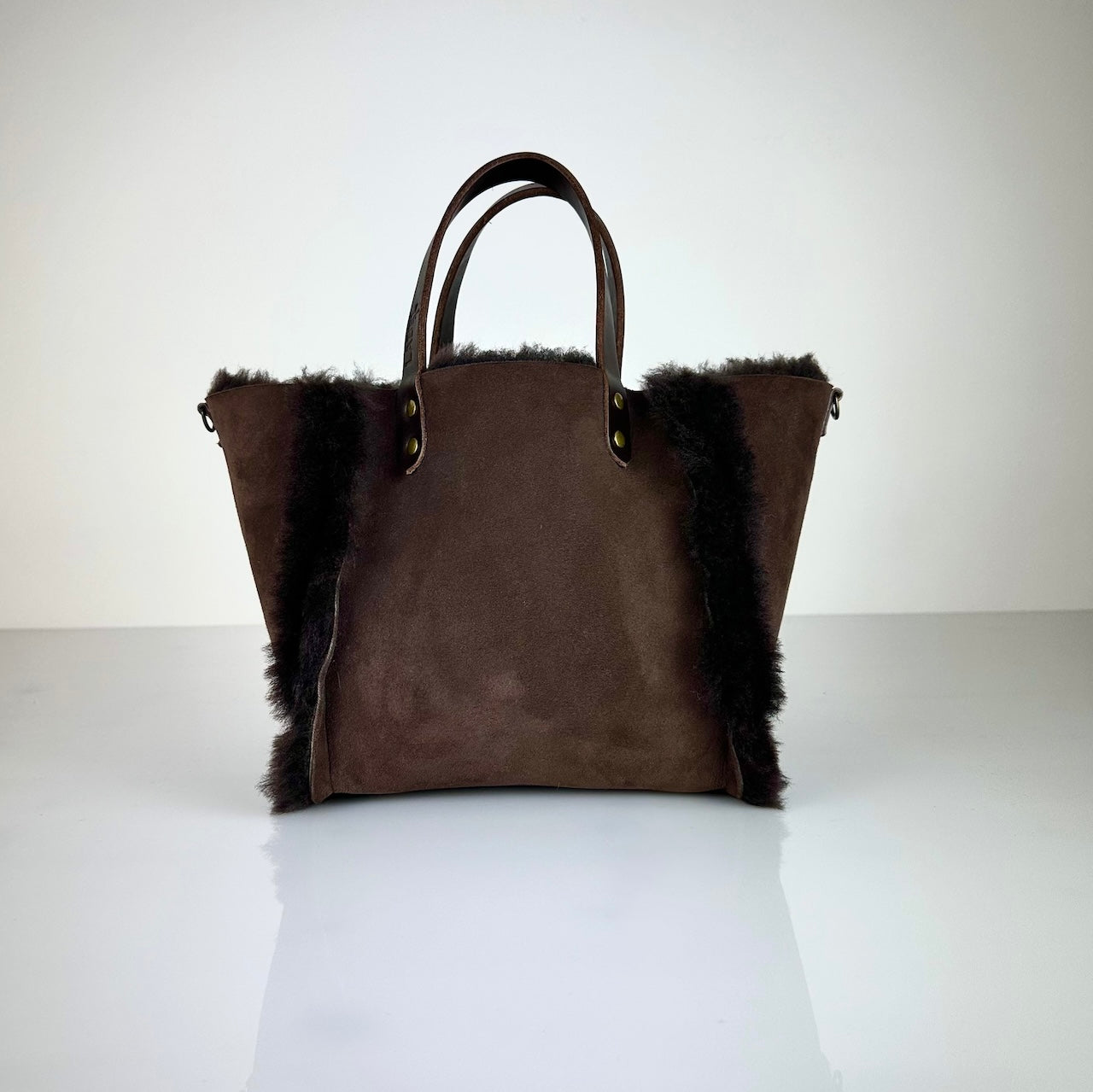 Die HANDBAG SHEARLING REVERSIBLE, MEDIUM von LABEL17 wird aus luxuriösem Merino-Lammfell gefertigt, das der Tasche einen einzigartigen und stilvollen Look verleiht. Mit dunkelbraunen Griffen aus Sattlerleder und einem abnehmbaren Schulterriemen bietet sie vielseitige Tragemöglichkeiten, egal ob in der Hand oder als Crossbody.
Diese reversible Tasche ist ein Meisterwerk der Schweizer Handwerkskunst und vereint schlichtes Design mit hochwertiger Sattlerarbeit. Jede Tasche ist ein Unikat. 